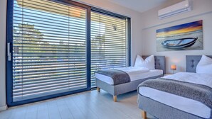 Une chambre avec deux lits, une grande porte-fenêtre coulissante et un tableau représentant un bateau accroché au mur.