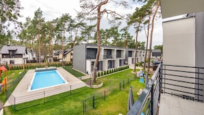 Un immeuble d’appartements moderne doté d’une piscine, entouré de pelouses et d’arbres bien entretenus.