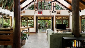 A spacious living area with a large window, a television, and a bookshelf. - Fern House your serene rainforest retreat (Bingil Bay)