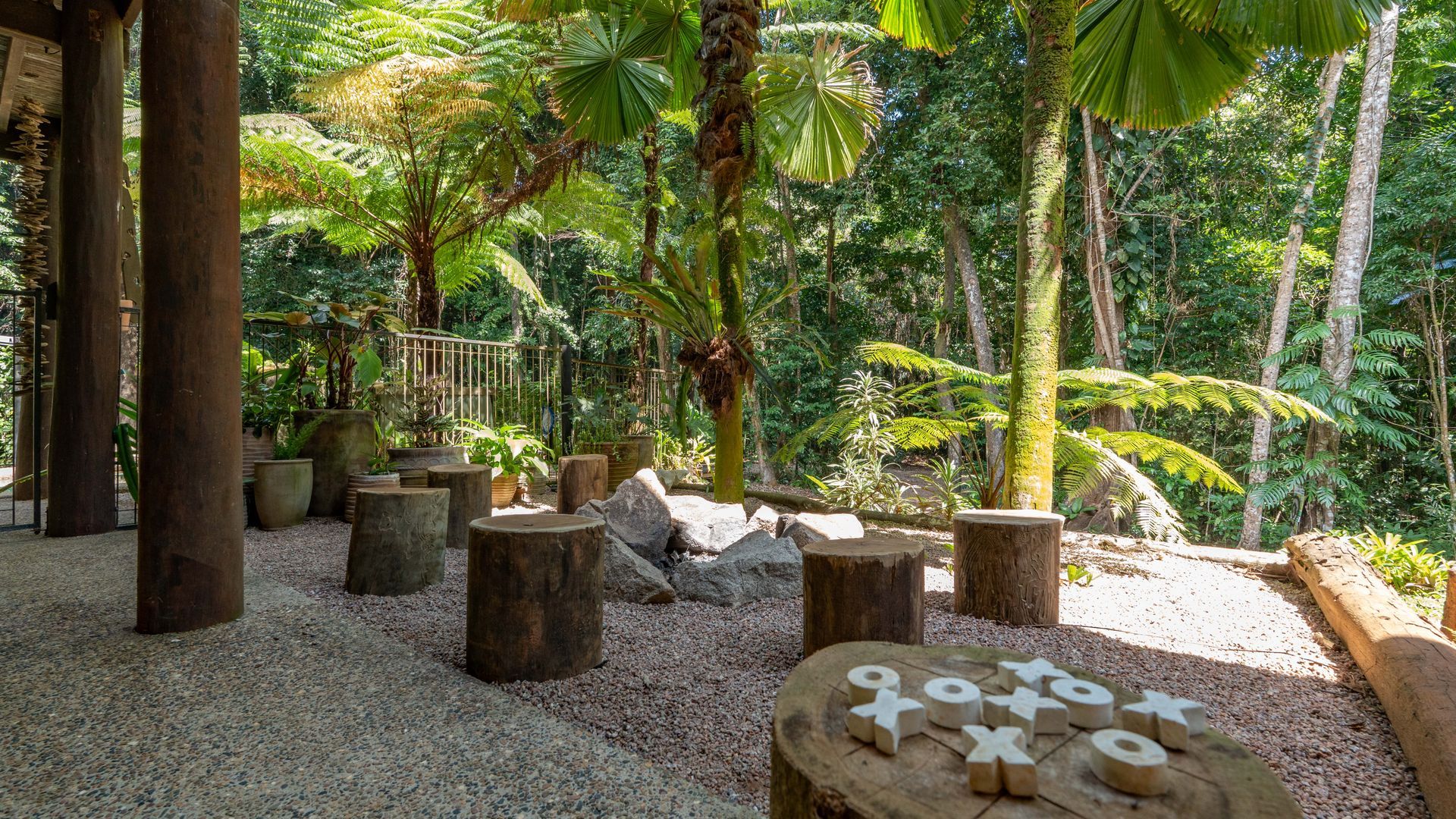 Un jardín tropical con asientos de piedra, palmeras y una valla de madera.