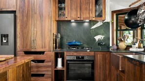 A kitchen with wooden cabinets, a built-in oven, and a gas stove. - Fern House your serene rainforest retreat (Bingil Bay)