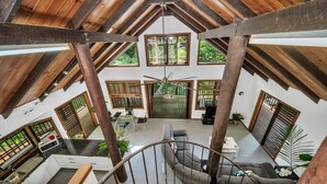 Ein geräumiger Loft mit hohen Decken, Holzbalken und großen Fenstern mit Blick auf Grünflächen.