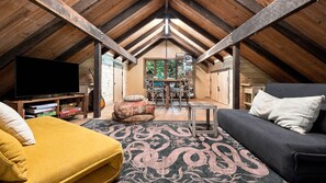 A cozy attic room with a wooden ceiling, a television, a sofa, a coffee table, and a patterned rug.