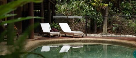 Un área de piscina con dos sillas de descanso y una terraza de madera.
