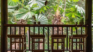 Un balcón de madera con vistas a follaje tropical y una barandilla de madera rústica.