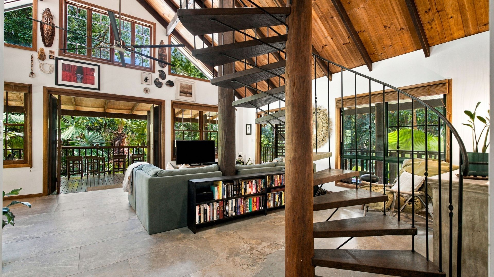 Amplia sala de estar con una gran estantería, un espacio de descanso cómodo y una escalera que conduce a un nivel superior.