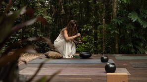 A person in a white dress kneeling on a wooden deck with a meditation mat, surrounded by greenery. - Fern House your serene rainforest retreat (Bingil Bay)