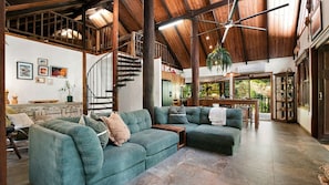 A spacious living area with a large green sectional sofa, a wooden staircase, and a view of the outdoors. - Fern House your serene rainforest retreat (Bingil Bay)