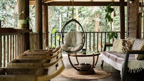 A wooden deck with a hanging chair, a woven bench, and a sofa with patterned cushions. - Fern House your serene rainforest retreat (Bingil Bay)