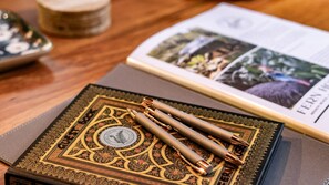 A book with ornate cover design, a pen, and a magazine on a wooden surface. - Fern House your serene rainforest retreat (Bingil Bay)