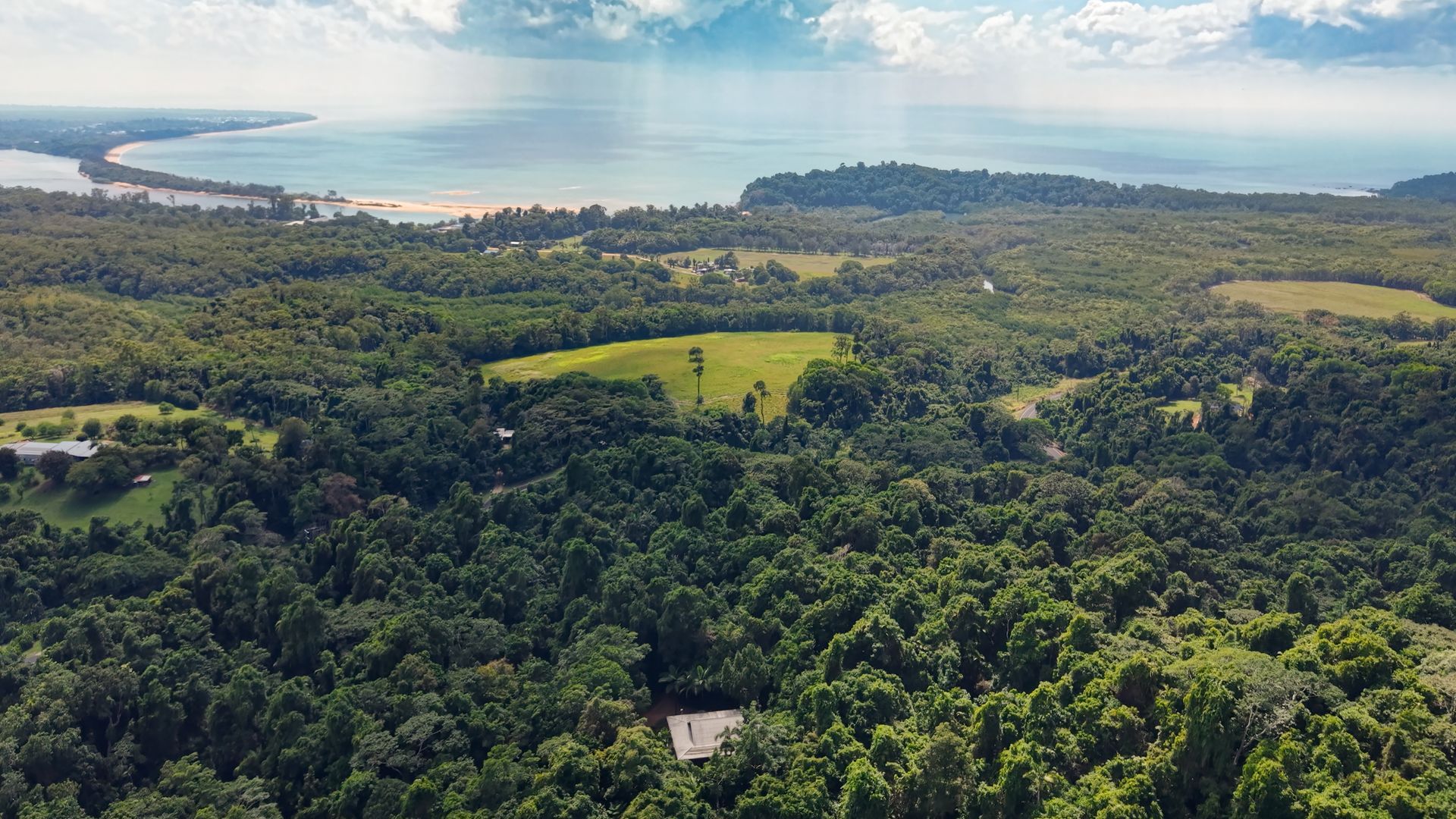 Paesaggio lussureggiante con fitta vegetazione, un campo da golf e una spiaggia in lontananza.