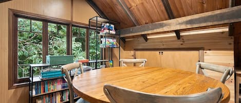 Un intérieur en bois avec une table ronde et des chaises, des étagères et une vue dégagée grâce à de grandes fenêtres.