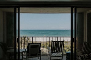 A balcony with a view of the ocean, featuring two wooden chairs and a small table.
