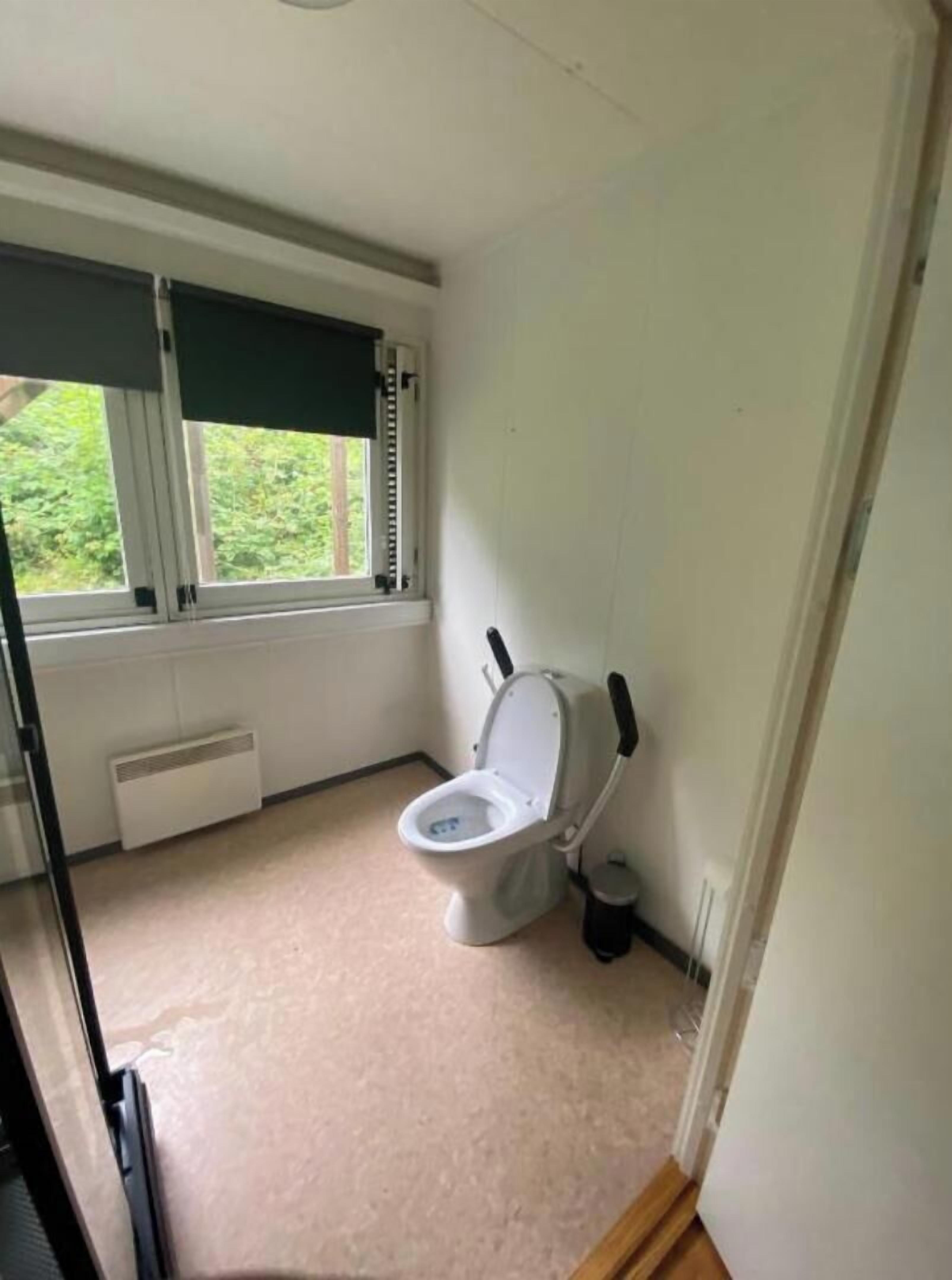 A small bathroom with a toilet, a window with blinds, and a radiator.