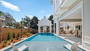 Un espace piscine moderne avec une piscine à l’eau d’un bleu limpide, des chaises longues blanches et une structure de type gazebo également blanche.