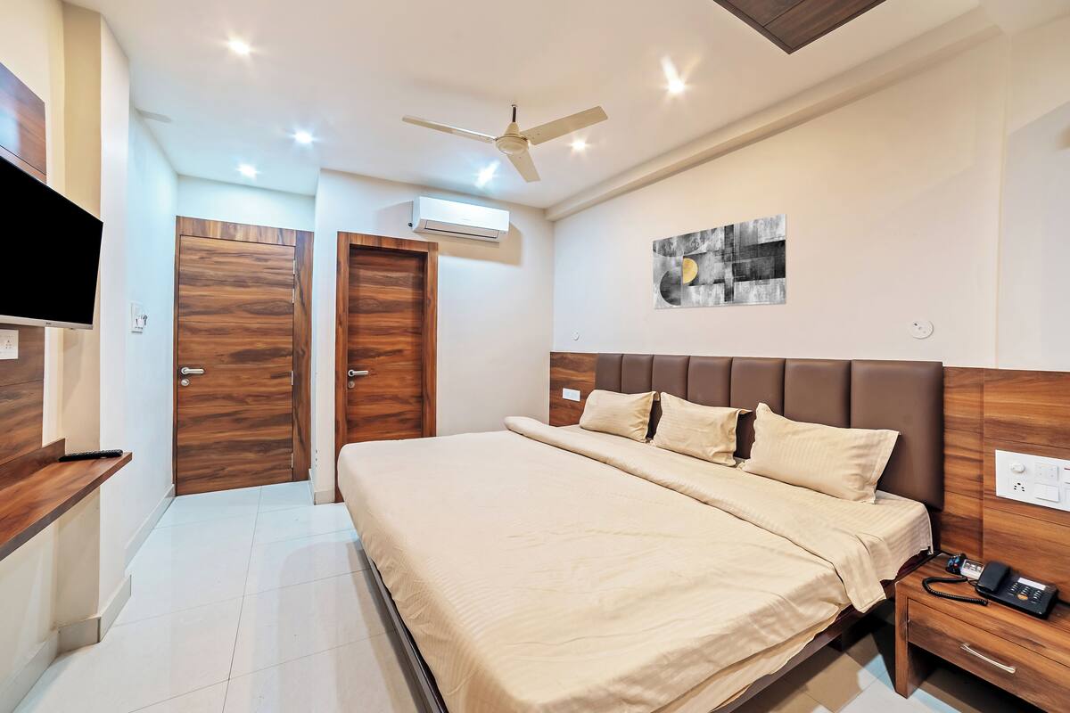 A modern hotel room with a large bed, a bedside table, a ceiling fan, an air conditioning unit, and a wall-mounted TV.