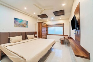 Un dormitorio moderno con una cama grande, un ventilador de techo, un televisor montado y una ventana con vistas.
