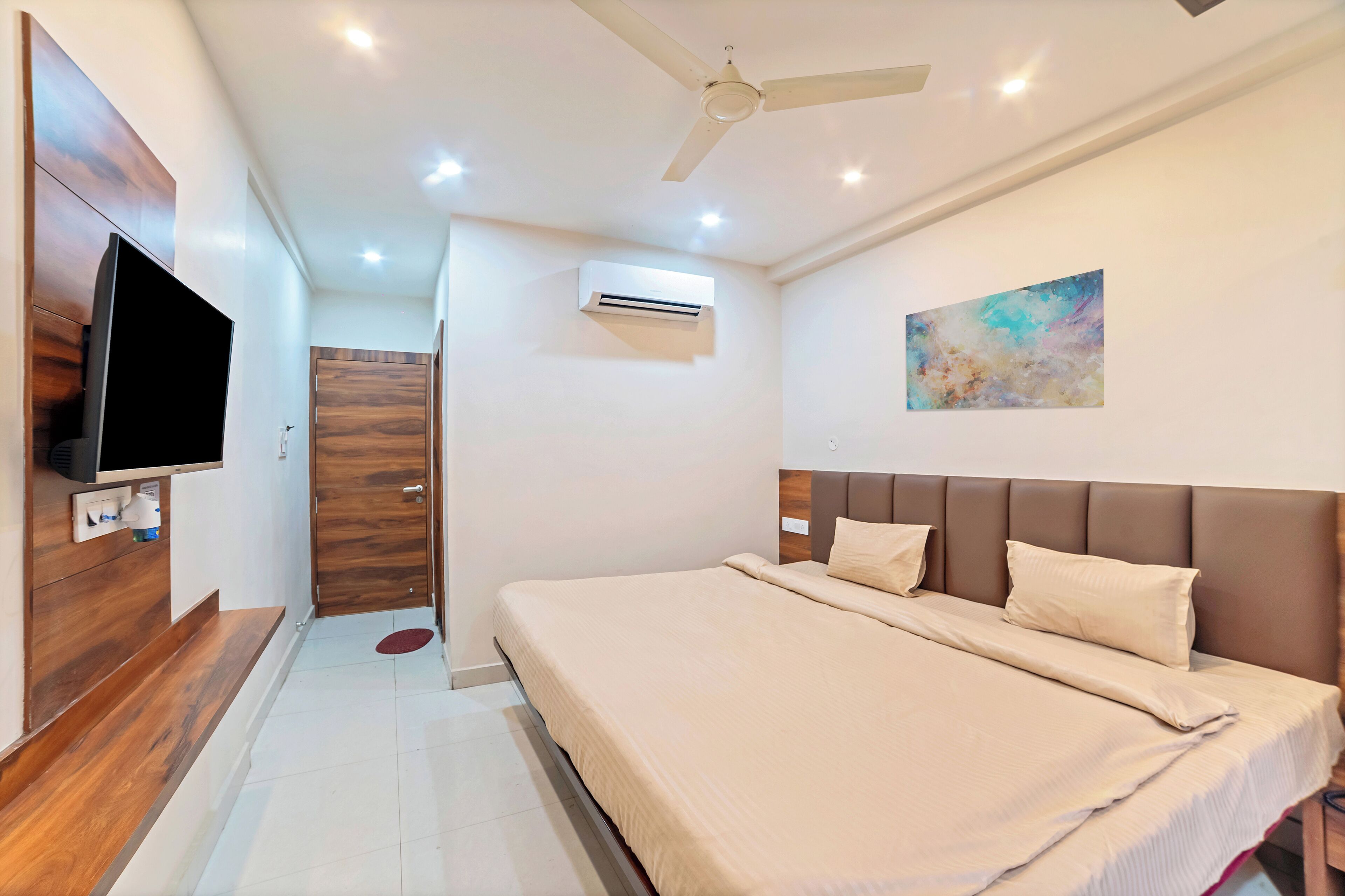 A modern bedroom with a large bed, a flat-screen TV, an air conditioning unit, and a ceiling fan.