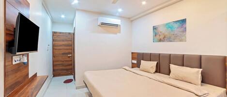 A modern bedroom with a large bed, a flat-screen TV, an air conditioning unit, and a ceiling fan.