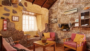 Un salon rustique avec des murs en pierre, un plafond en bois, une cheminée, un canapé, deux fauteuils et une table basse.