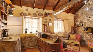 Une cuisine rustique avec des murs en pierre, des poutres en bois, un bar intégré et un évier en pierre.
