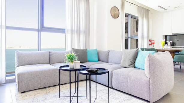A modern living room with a grey sectional sofa, two round black tables, and a view of the sea through large windows. - Bloomfields Modern STU Pixel Beach Acces (Abu Dhabi)