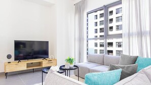A modern living room with a flat-screen TV, a sofa, a coffee table, and a large window with curtains. - Bloomfields Modern STU Pixel Beach Acces (Abu Dhabi)
