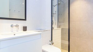 A modern bathroom with a glass-enclosed shower, white tiles, and a large mirror above the sink. - Bloomfields Modern STU Pixel Beach Acces (Abu Dhabi)