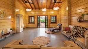 A log cabin interior with a fireplace, leather sofas, a ceiling fan, and a view through the glass door. - Villa 199 Amarja's Sunset Retreat (Mawal)