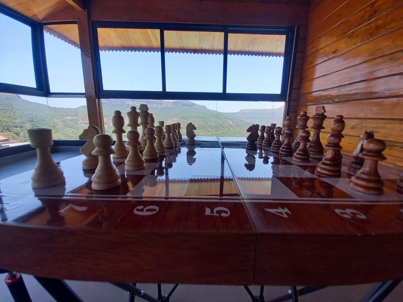 Un jeu d’échecs est installé sur une table, et de larges fenêtres offrent une vue sur un paysage montagneux.