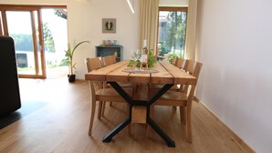 A dining area with a wooden table, chairs, and a central black metal support. There is a potted plant and a shelf with decorative items in the background. - Holiday Home in Dabie, Directly at the Lake (Bytow)