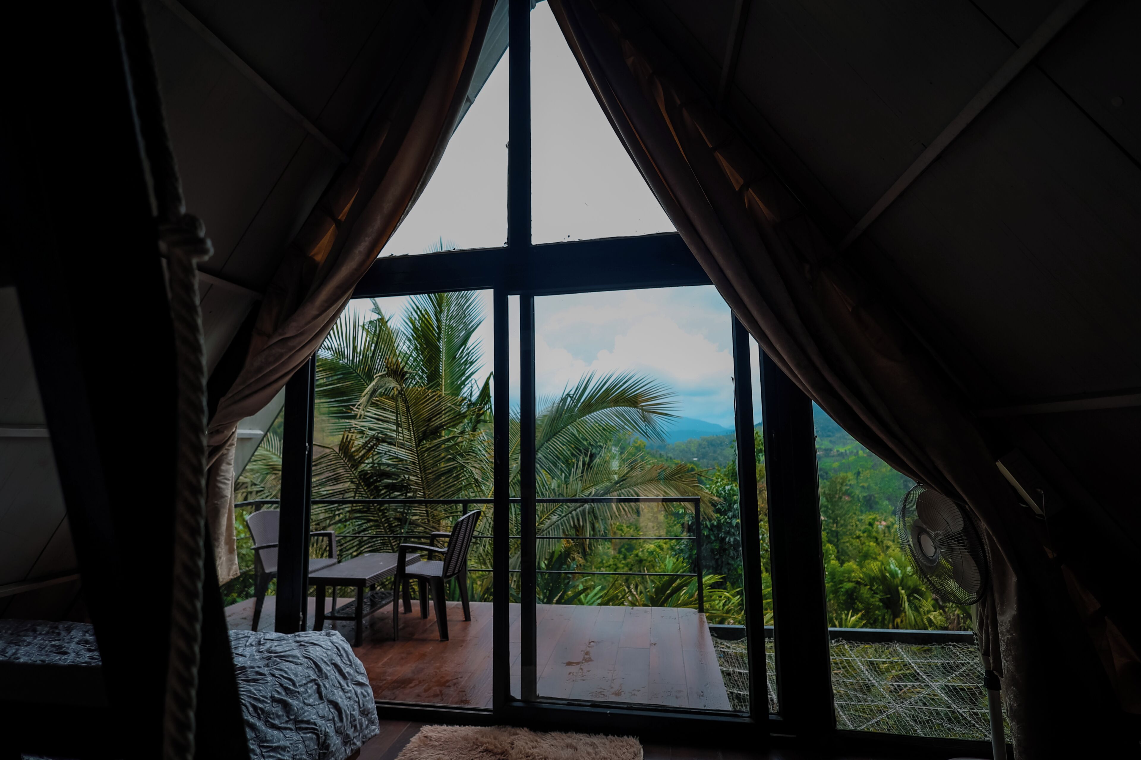 Una habitación con un amplio ventanal corredera que da a un balcón con vistas a exuberante vegetación y montañas.