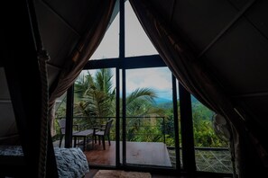 Una habitación con un amplio ventanal corredera que da a un balcón con vistas a exuberante vegetación y montañas.