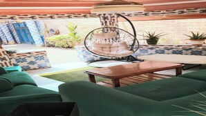 Un espace patio avec des canapés verts, un fauteuil suspendu et une table ronde.