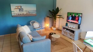 Een woonkamer met een bank, een televisie, een plant en een schilderij aan de muur.