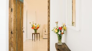 Un couloir avec une porte en bois, une petite table ornée de fleurs et un miroir accroché au mur.