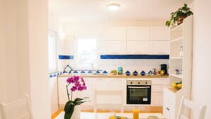Une cuisine moderne avec des meubles blancs, un pare-feu bleu et un coin repas où une table est dressée pour le petit-déjeuner.