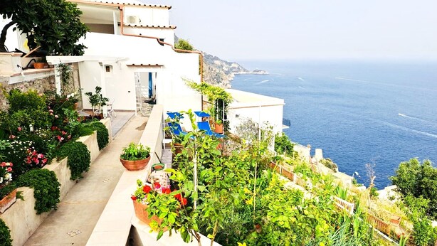 Un bâtiment situé sur la côte, doté d’un balcon donnant sur la mer, de plantes en pot et d’un espace salon extérieur.