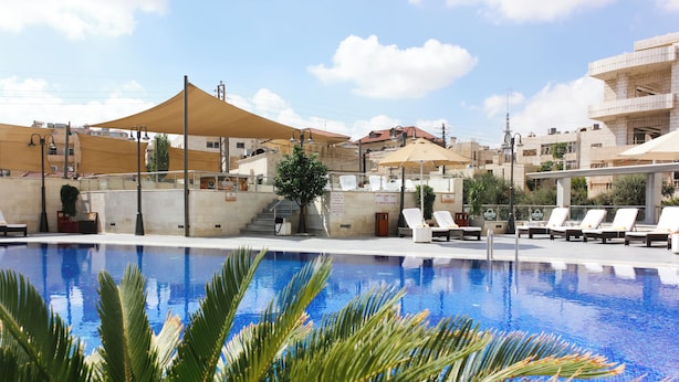Una piscina con tumbonas y sombrillas, rodeada de edificios y una escalera.