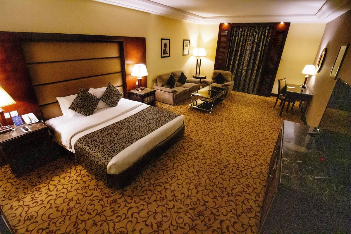 A hotel room with a large bed, a sofa, a coffee table, a desk, and two lamps.