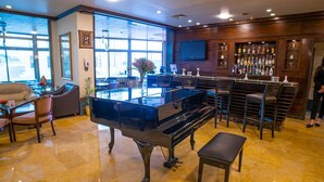 Amplia habitación con un piano de cola, una zona de bar con diversas botellas de licores y un amplio ventanal que proporciona luz natural.