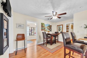 A dining area with a wooden table and chairs, a ceiling fan, and framed artwork on the walls. - Walk to Beach & Old Town - Bay St. Louis Retreat (Bay St Louis)