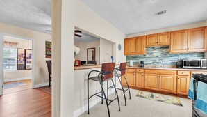 Cocina con armarios de madera, un microondas y dos taburetes de bar.