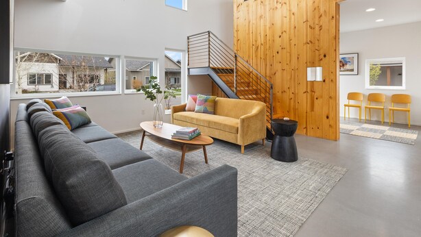 Una sala moderna con un sofá seccional gris, un sillón amarillo, una mesa de centro y una escalera que conduce a otro nivel.