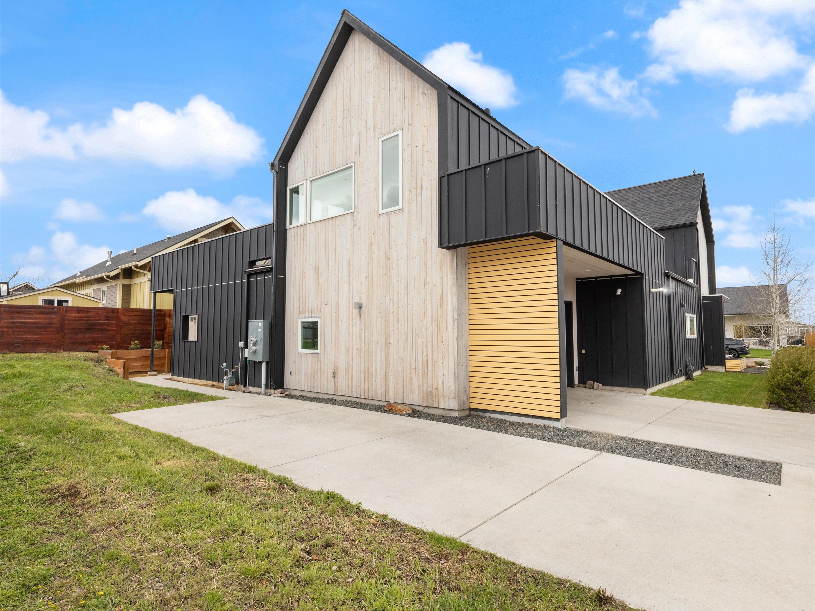 A modern two-story house with a sloped roof, large windows, and a combination of wood and metal siding.
