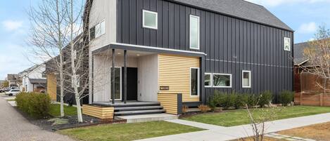 A modern two-story house with a dark exterior, a front porch, and a small front yard.