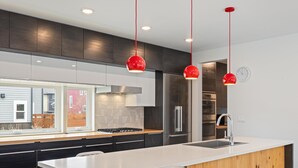 Una cocina moderna con una isla central, electrodomésticos de acero inoxidable e iluminación colgante roja.