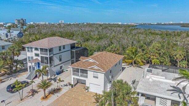 A two-story building with a flat roof, surrounded by palm trees and a body of water in the background. - 401 Pet-friendly, Pirate's Cove Retreat 3 Bedroom Home (Fort Myers Beach)