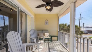 A covered porch with two Adirondack chairs, a small table, and a ceiling fan. - 401 Pet-friendly, Pirate's Cove Retreat 3 Bedroom Home (Fort Myers Beach)