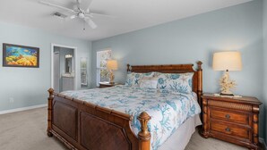 A bedroom with a wooden bed, a nightstand, a lamp, a ceiling fan, and a framed picture on the wall. - 401 Pet-friendly, Pirate's Cove Retreat 3 Bedroom Home (Fort Myers Beach)